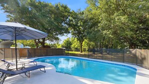 A swimming pool with lounge chairs and an umbrella, surrounded by trees and a fence. - Country Retreat home with Private pool,Near Orlando International Airport (Kissimmee)