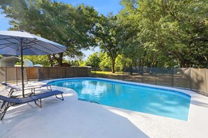 A swimming pool with lounge chairs and an umbrella, surrounded by trees and a fence. - Country Retreat home with Private pool,Near Orlando International Airport (Kissimmee)