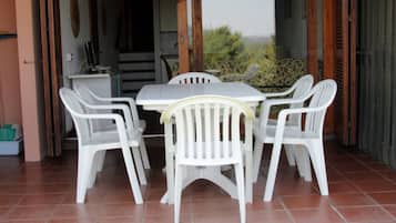 Eine Terrasse im Freien mit einem weißen Tisch und Stühlen, einem Fliesenboden und Blick auf Grünflächen.