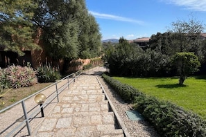 A stone staircase leading up to a building, surrounded by greenery and a clear sky.