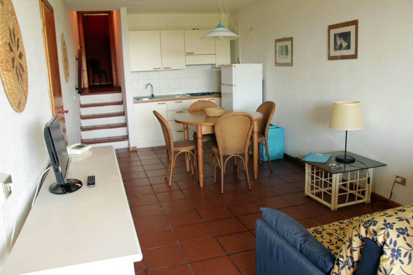 Un ambiente compatto con angolo cottura, zona pranzo e un letto con biancheria da letto a motivi floreali.