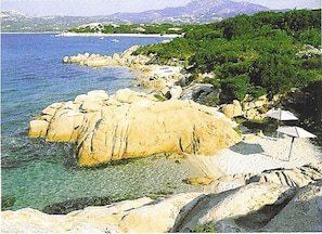 A coastal landscape with rocky formations, clear water, and greenery.