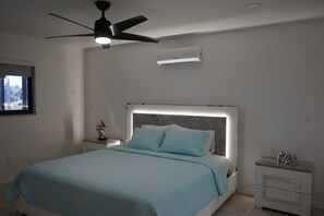 Une chambre à coucher avec un lit, une table de chevet, un ventilateur de plafond et une fenêtre.
