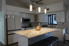 Une cuisine moderne avec des meubles blancs, un îlot central doté de tabourets, un four à micro-ondes et des luminaires suspendus.