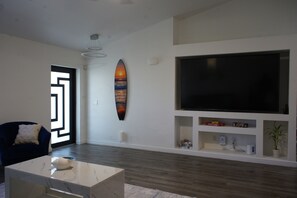 A modern living room with a large flat-screen TV, a decorative surfboard, and a minimalist design. - Our Serenity Cove with a private pool in Cape Coral. (Cape Coral)