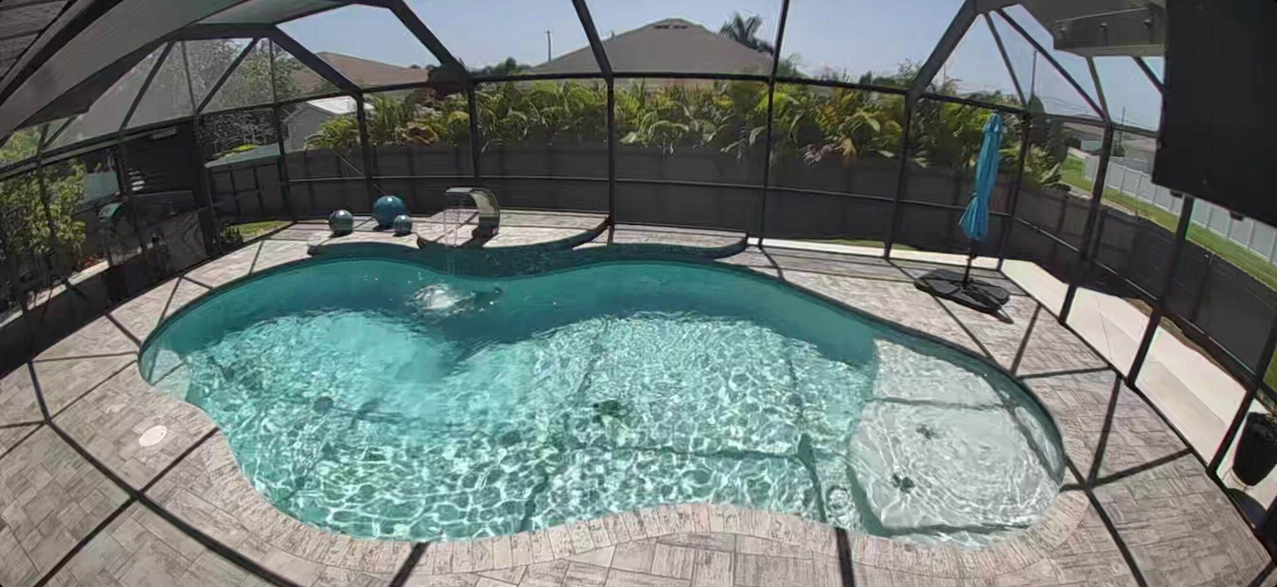 Piscina circular con agua cristalina, rodeada por un porche cubierto que ofrece vista a una zona residencial.