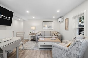 A modern living room with a sofa, coffee table, and a TV mounted on the wall. - North End 1BR/1BA Unit 3 - Walk to Beach & Boardwalk (Ocean City)