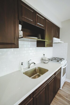 A kitchen with dark wooden cabinets, a white countertop, a stainless steel sink, a gas stove, and a white tiled backsplash. - Finch Cottage - 2-Bedrooms - Family Friendly (Trent Lakes)