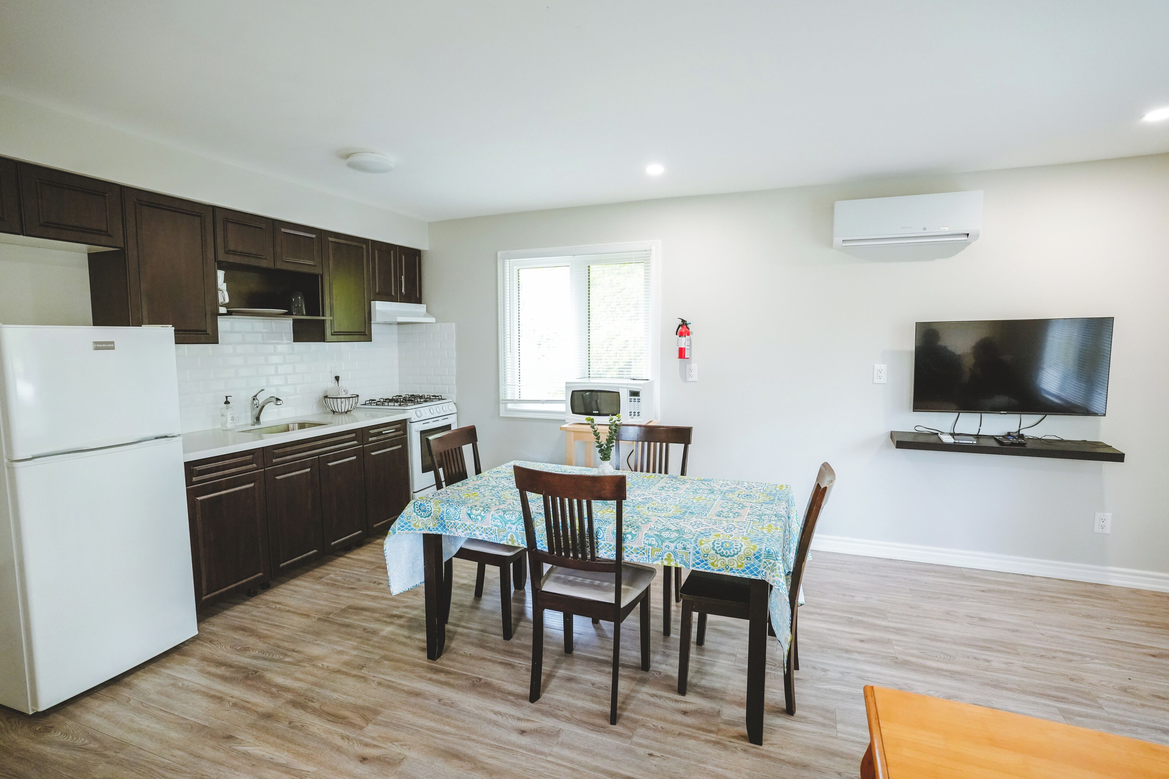 A compact kitchen with a dining area, a television, and a fire extinguisher.