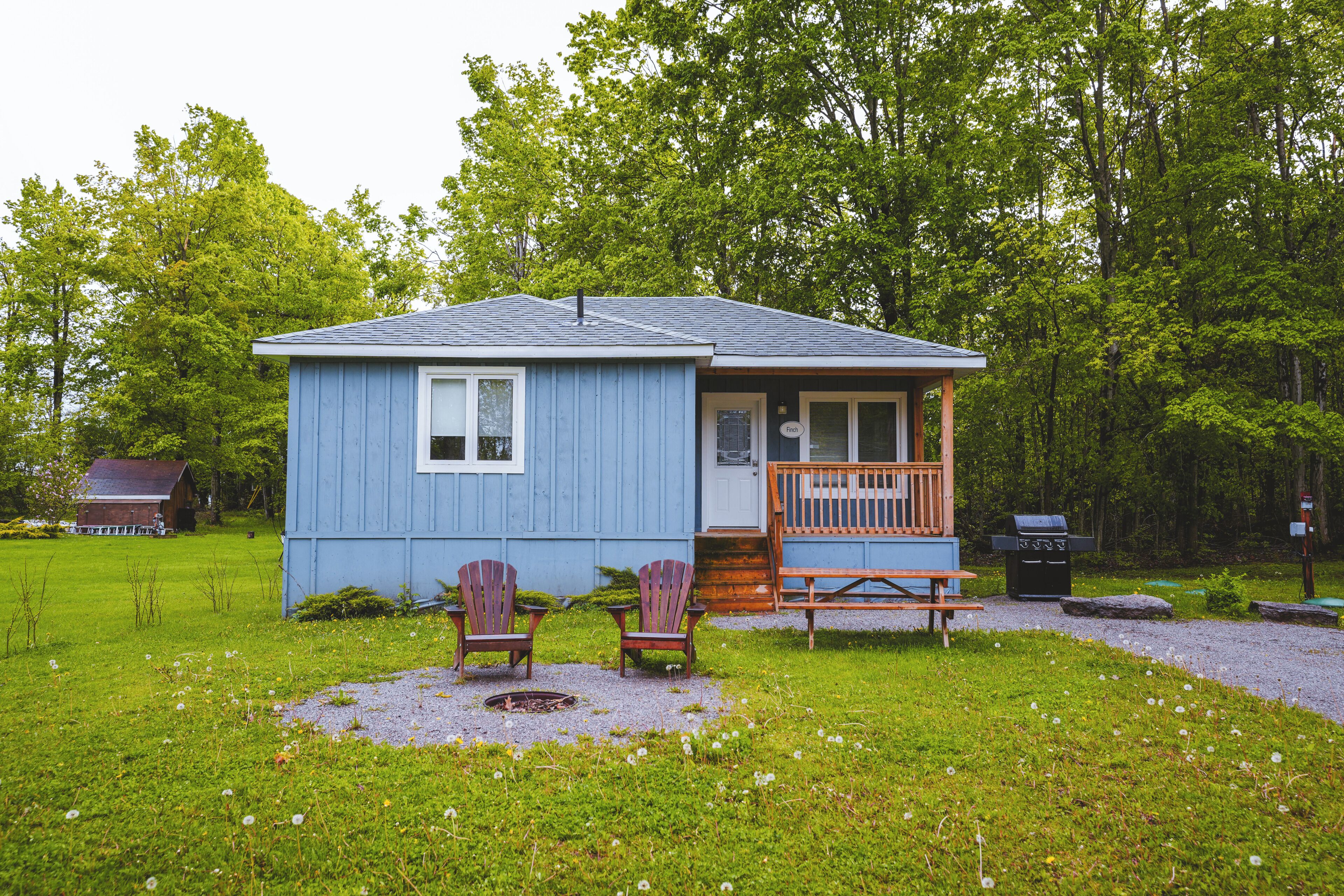 Une petite cabane bleue avec une véranda, deux fauteuils Adirondack et un barbecue.