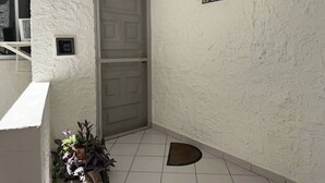 Eine Raumecke mit weißer Wand mit Struktur, einer geschlossenen Tür, einem kleinen Topfpflanzen und einem an der Wand befestigten Schild.
