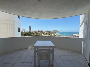 Ein Balkon mit weißem Tisch und Stuhl, der Blick auf das Meer und die Bebauung bietet.