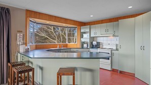 Cocina moderna con isla central, armarios de madera y un ventanal con vistas a árboles.