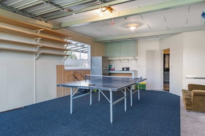 A room with a ping pong table, a kitchen area, and a seating area with a chair.