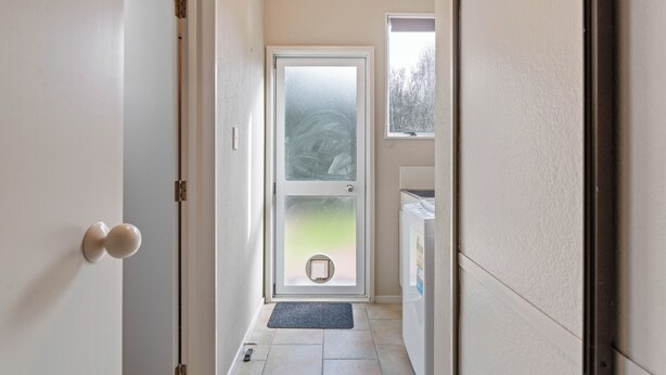 Un pasillo que conduce a una puerta con un ventanal esmerilado, un timbre y una lavadora al fondo.