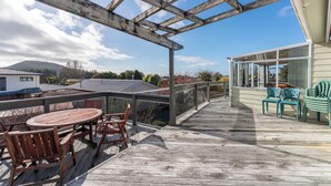 Una terraza de madera con pérgola, mobiliario exterior y vistas a casas al fondo.