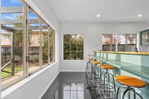 Uma cozinha moderna com grandes janelas, um espaço bar com banquetas e vista para o quintal.