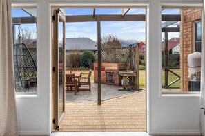 A patio area with a brick floor, wooden furniture, and a barbecue grill. - Meadowstone Vista - Wanaka Holiday Home (Wanaka)