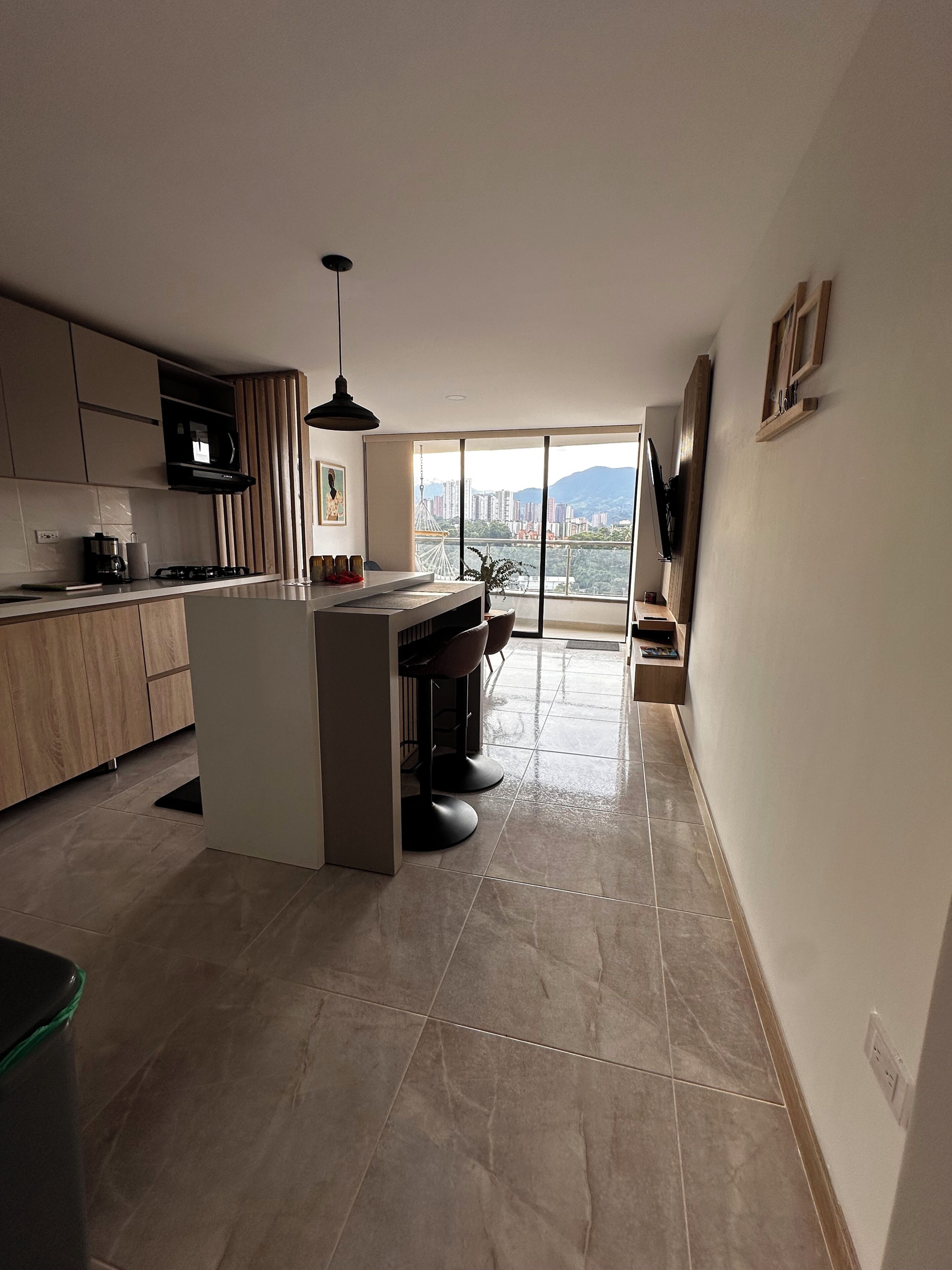 A modern kitchen with a central island, a dining area with chairs, and a large window offering a city view.