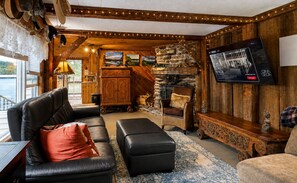 A cozy cabin interior with a stone fireplace, leather furniture, and a television mounted on the wall.