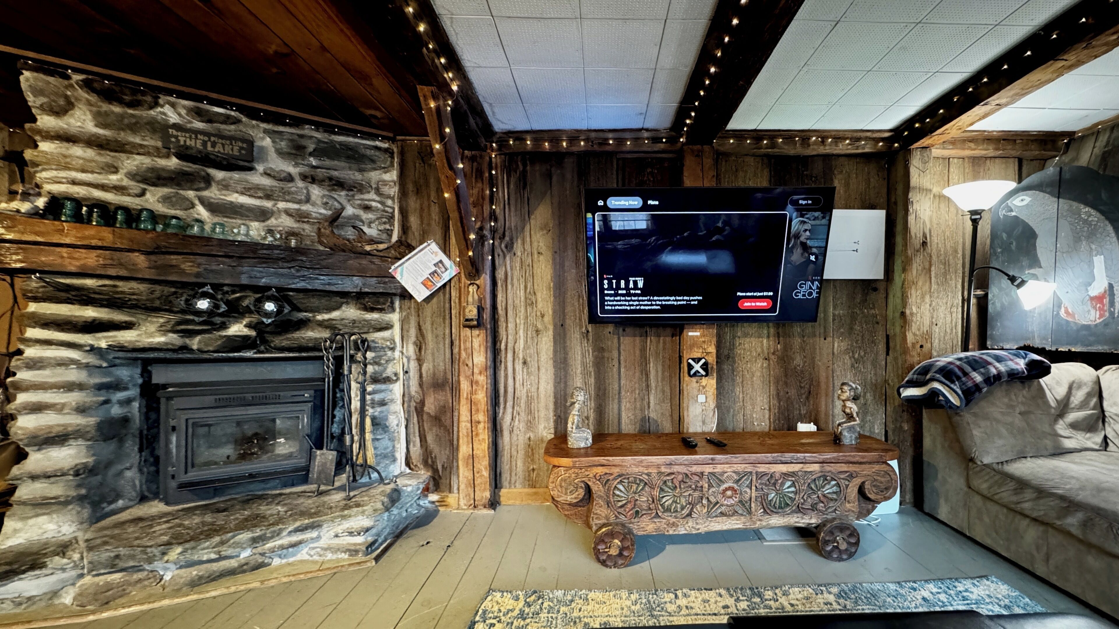 Un interior rústico con pared de piedra, chimenea, banco de madera y televisor de pantalla plana fijado a la pared.