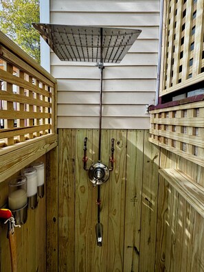 A wooden outdoor shower with a metal spout and a rain cover.
