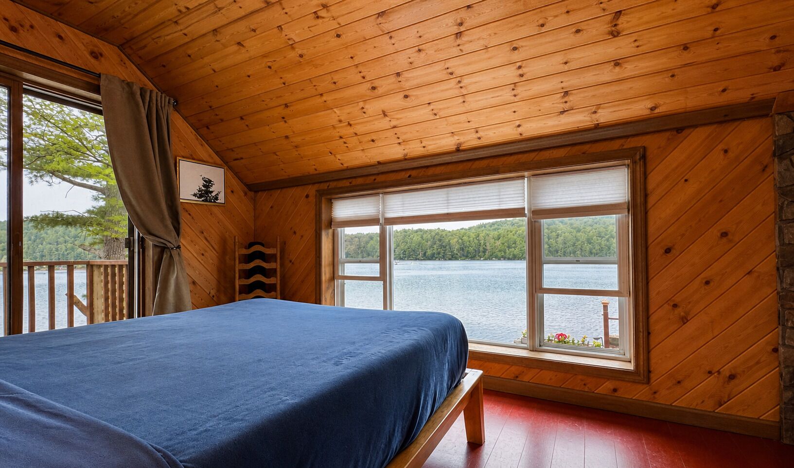 Una habitación tipo cabaña con una cama, una ventana con persianas, techo de madera y vista a un lago.