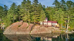 A cabin with a dock, surrounded by dense forest and a large rock formation.