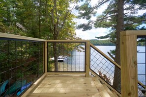 A wooden deck with a metal railing overlooking a lake, surrounded by trees.