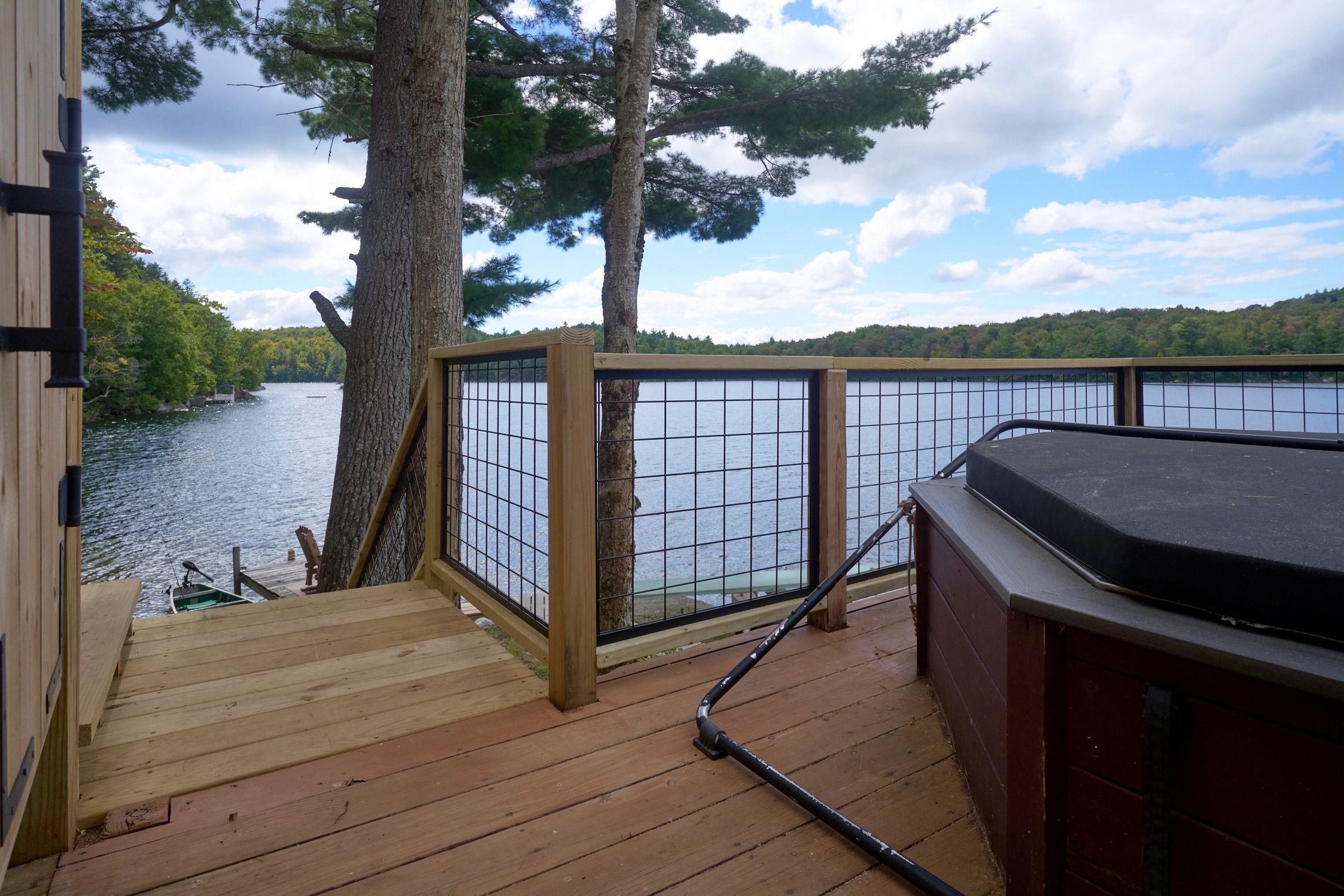 A wooden deck with a hot tub and a view of a lake surrounded by trees.