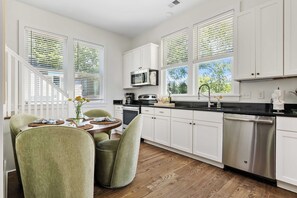 Una cocina moderna con armarios blancos, electrodomésticos de acero inoxidable y una zona de comedor con sillas verdes y una mesa de madera.