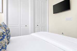 A hotel room with a bed, a television mounted on the wall, and a white door. - Brand New - Downtown 2 Bedroom (Charleston)