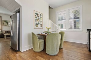 Un comedor con una mesa de madera, sillas tapizadas de verde y un refrigerador.
