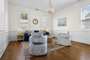 Un salon avec un canapé bleu, des poufs à motifs, un miroir rond et un tableau accroché au mur.