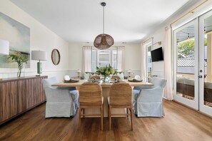 A dining area with a wooden table, four grey upholstered chairs, a woven pendant light, and a view of the outdoors through a glass door.