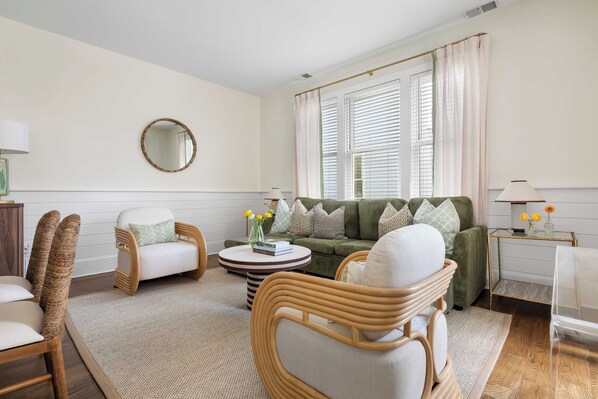 A living room with a sofa, chairs, a coffee table, and a round mirror on the wall.