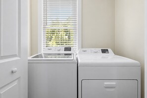 A laundry room with a front-loading washer and dryer, a window with blinds, and a door. - Spacious 4bd w. Balconies, Heart of Downtown! (Charleston)