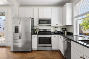 Una cocina moderna con electrodomésticos de acero inoxidable, armarios blancos y piso de madera.