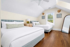 A bedroom with two beds, a ceiling fan, a window with blinds, and a mirror.