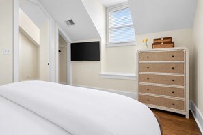 Un dormitorio con cama, cómoda, televisor y ventana con persianas.