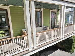 A covered porch with a white railing, green siding, and a seating area with cushions. - Spacious 4bd w. Balconies, Heart of Downtown! (Charleston)