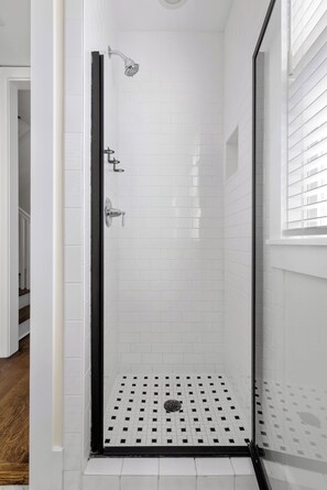 A glass-enclosed shower with white tiled walls and a black floor.