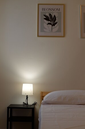 Habitación de hotel con cama, mesita de noche con lámpara y un cuadro enmarcado en la pared.