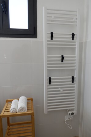 A bathroom with a white towel rack holding two towels, a wooden stool, and a window with a black frame. - La Casina in Massa: a house for 6 with parking, near the beach (Massa)