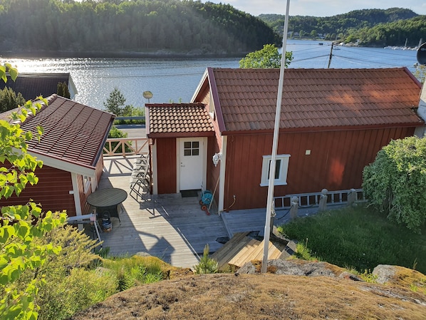 A wooden house with a red roof, a small porch, and a view of a lake.
