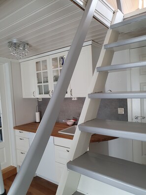 A kitchen with white cabinets, a wooden countertop, a sink, and a staircase.
