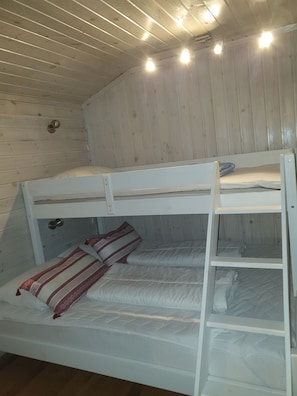 A bunk bed with two levels, a wooden ceiling, and a wall-mounted light fixture.