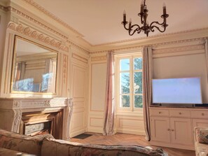 Une pièce avec une cheminée, un grand miroir, un téléviseur et une fenêtre avec des rideaux.