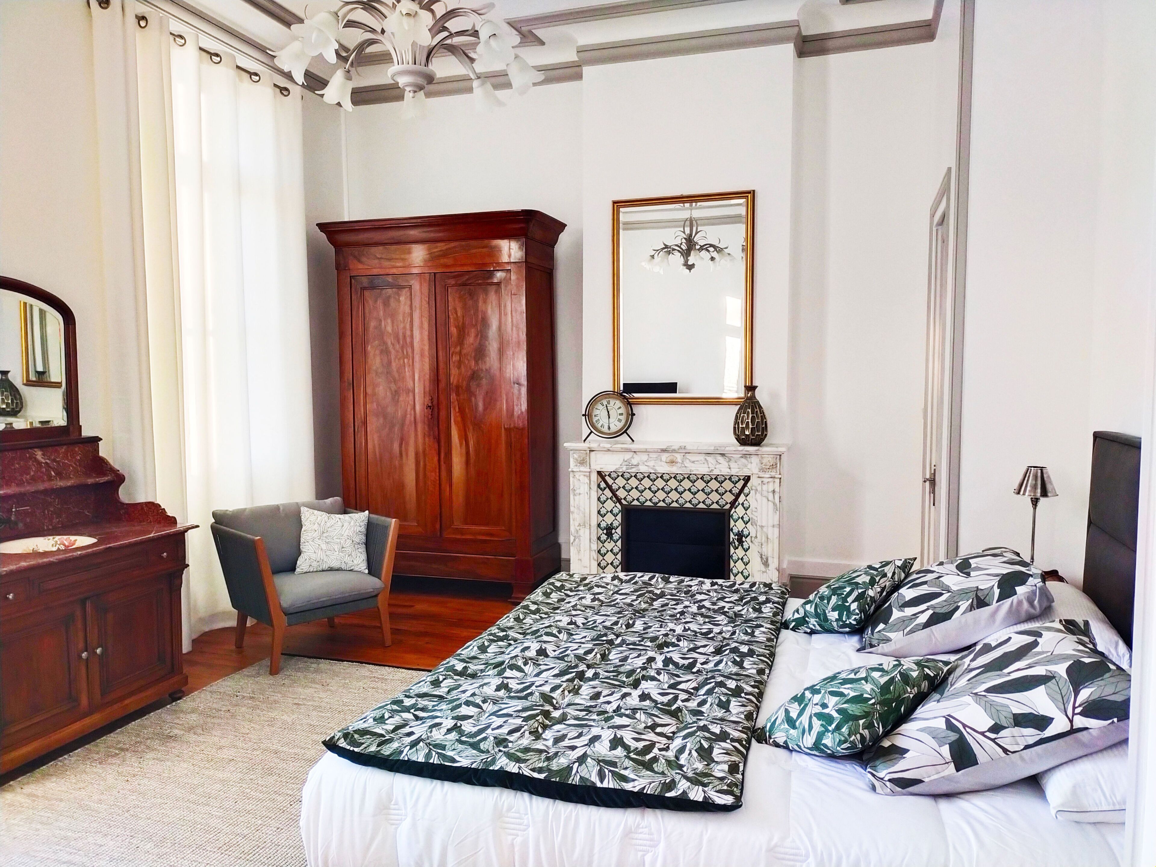 Une chambre à coucher avec un lit, une armoire en bois, une chaise, une cheminée et un miroir.