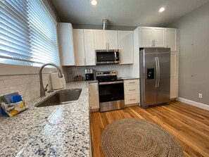 A kitchen with white cabinets, stainless steel appliances, a granite countertop, and a wooden floor. - The Fold at Reynolds Mountain | Asheville 10 Townhomes, Hot Tubs, Sleeps 80 (Asheville)